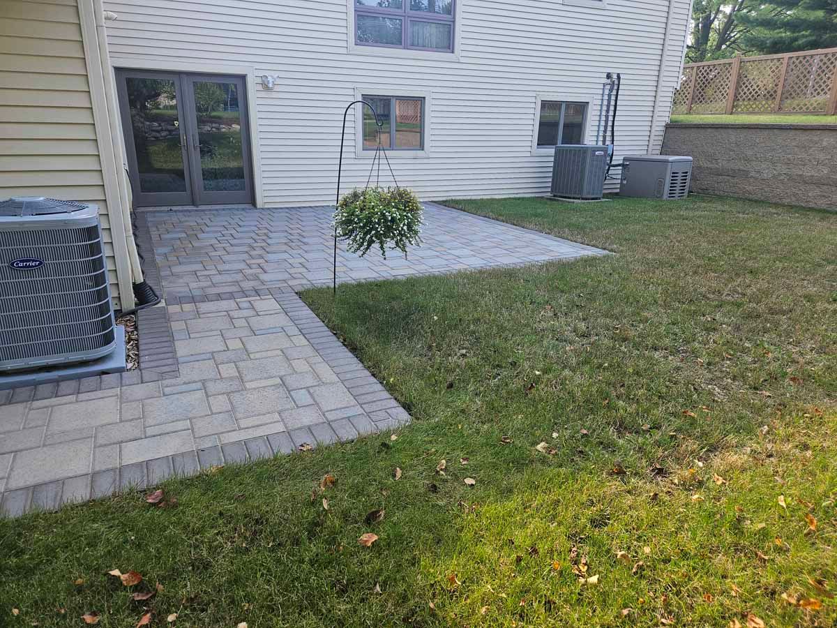 Back patio with stone pavers, small planted bed, sliding door, air conditioner units, and grassy yard