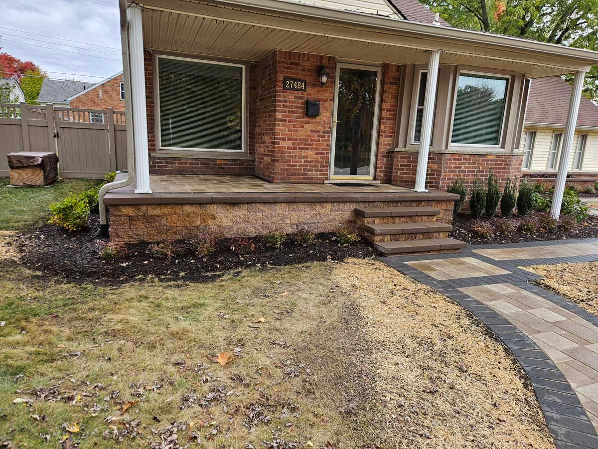 Brick house front porch with steps, windows, and a landscaped yard with curved stone walkway.