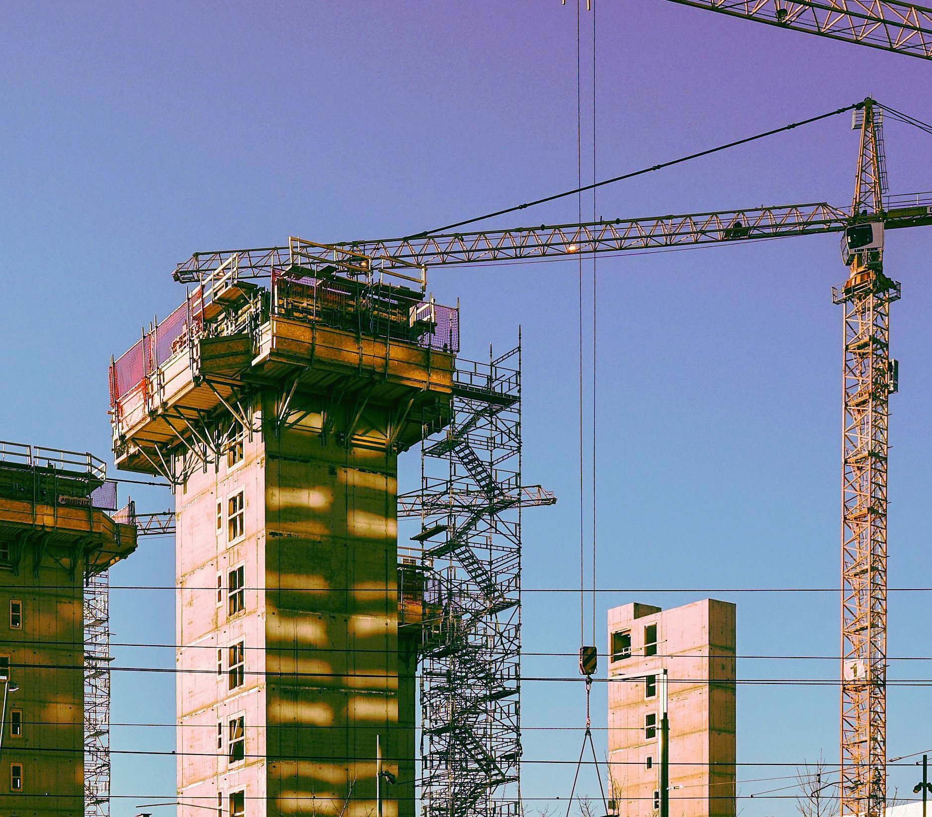 Construction site with tall concrete towers, cranes, and scaffolding against a purple sky