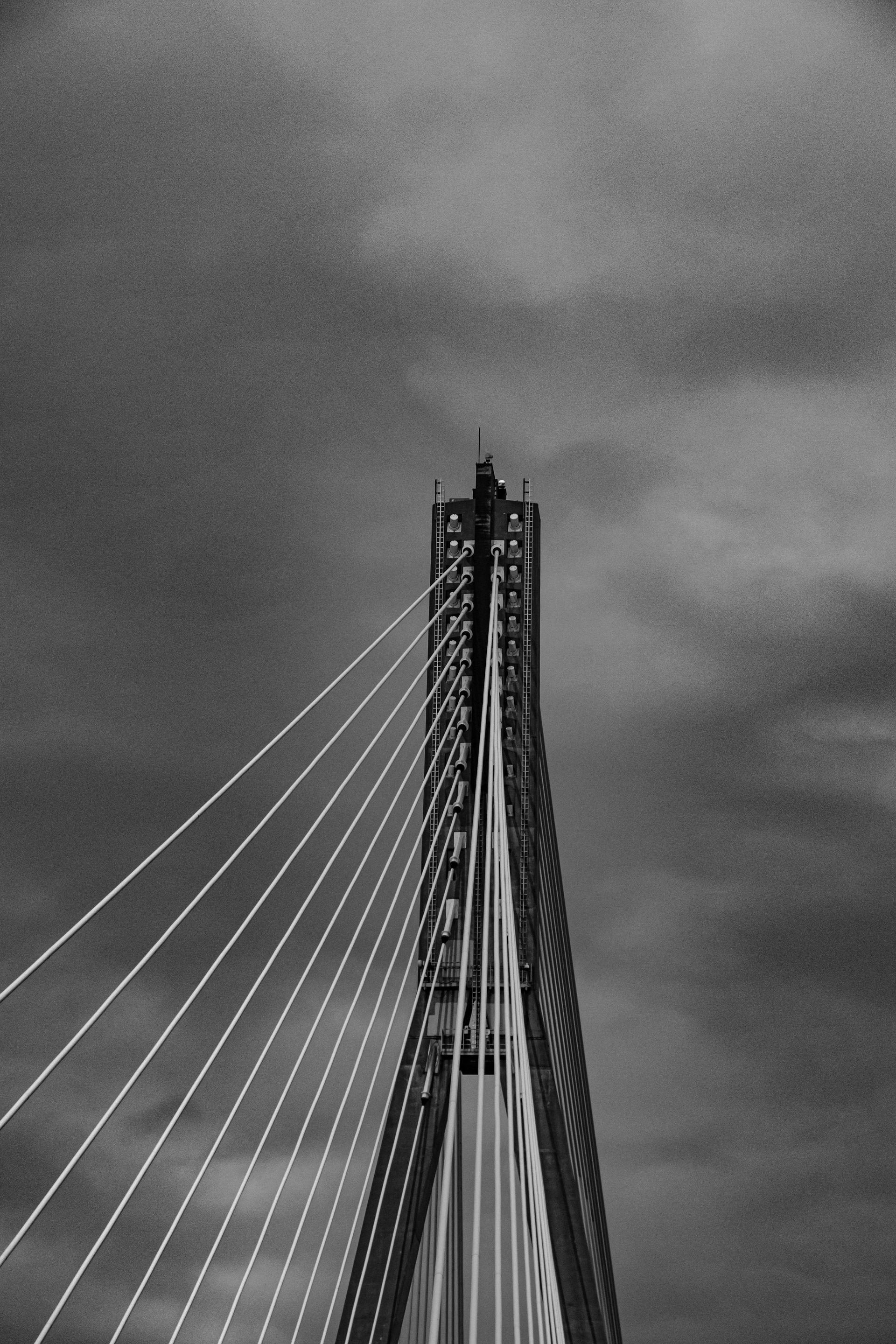 Monochrome view of a suspension bridge tower with cables against a cloudy sky