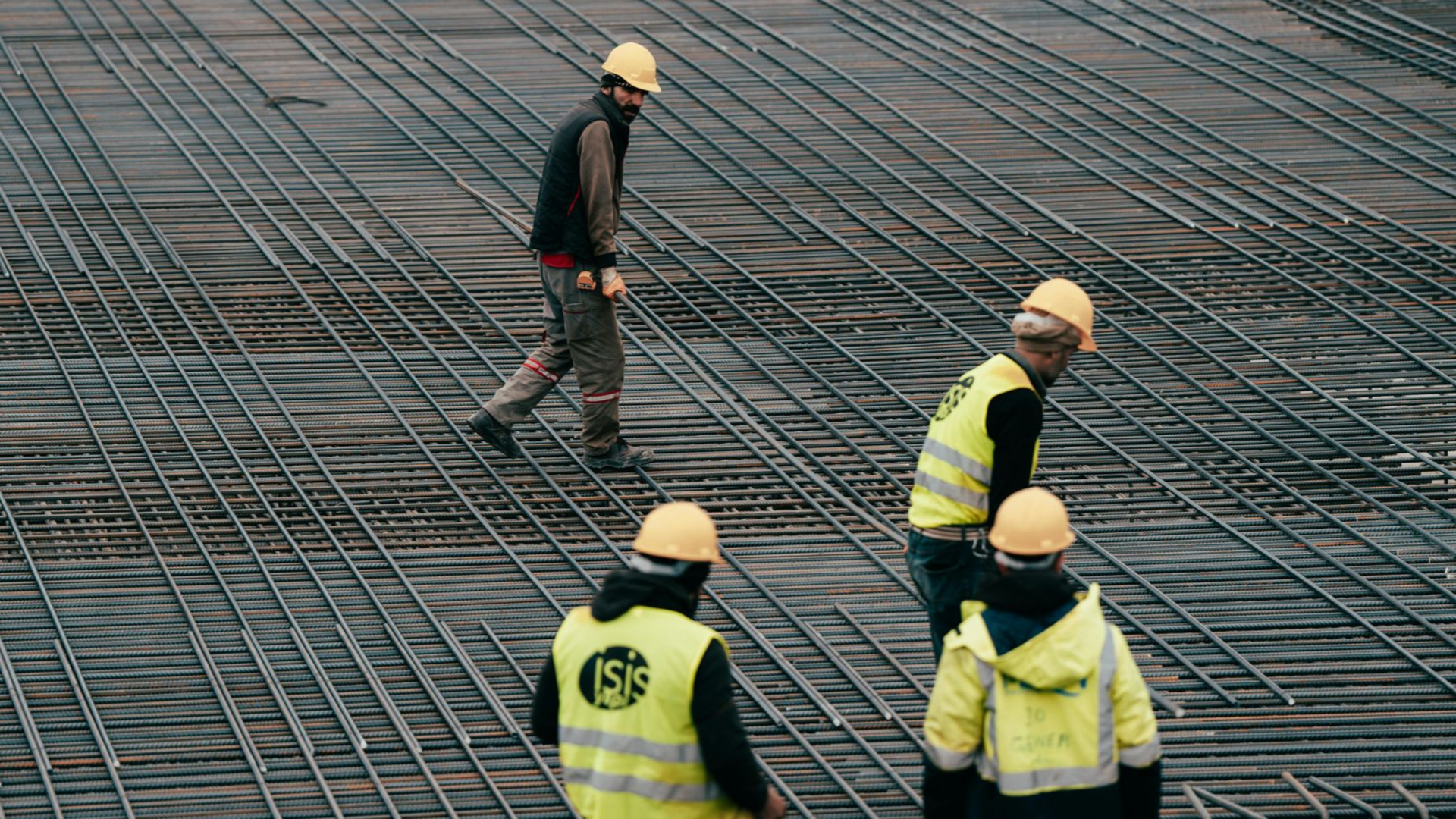 Construction workers in yellow vests and helmets standing on a steel rebar grid at a building site