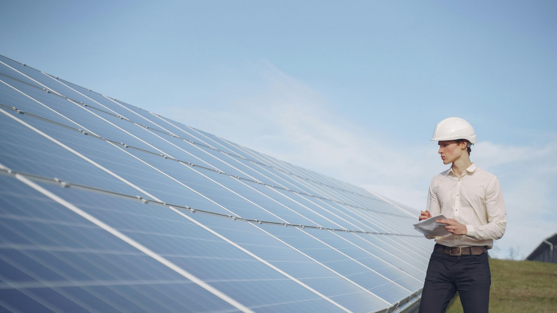 Engineer in white hard hat inspecting solar panels outdoors under a clear sky