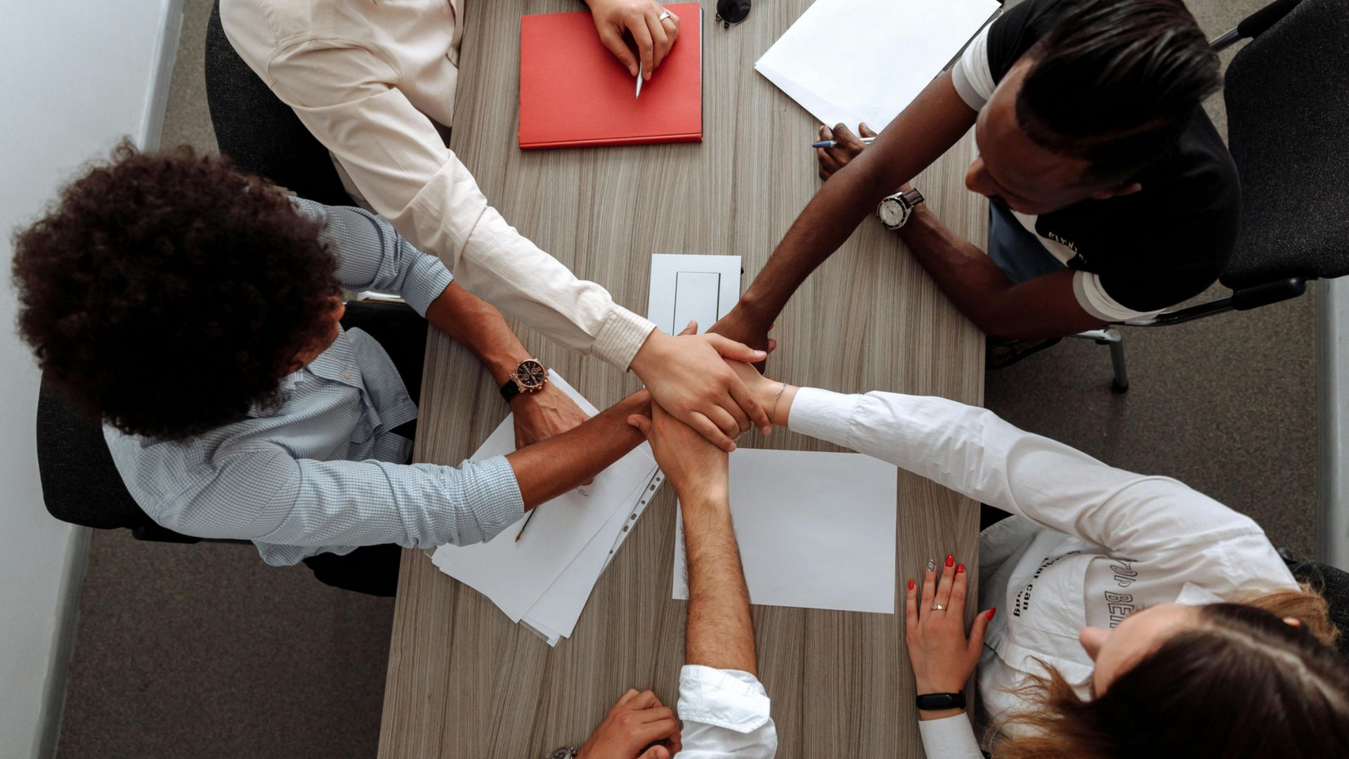 Colleagues stacking hands over papers at a conference table, showing teamwork and collaboration