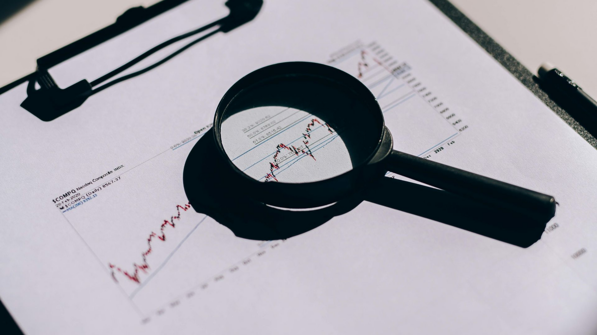 Magnifying glass over printed charts and graphs on a white desk, suggesting financial analysis