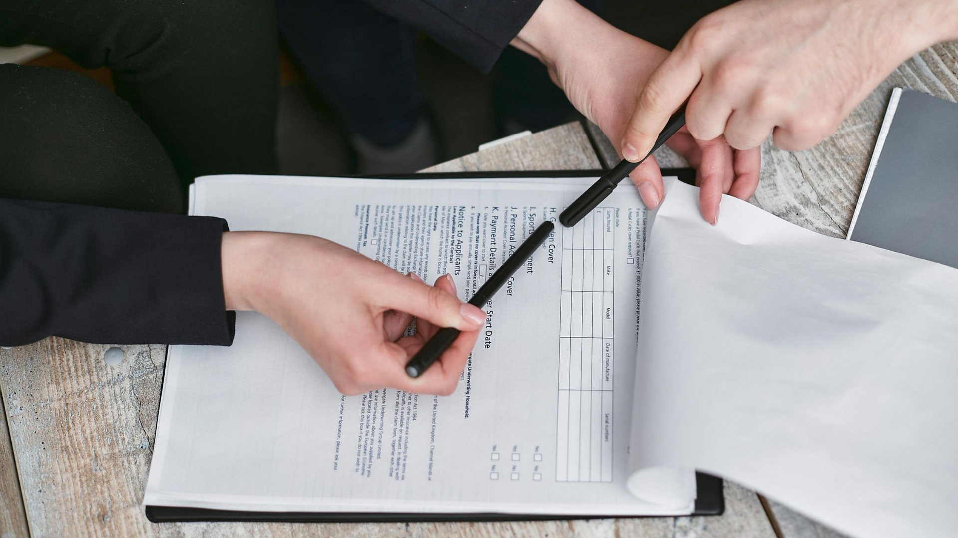 Hands and a pencil reviewing paperwork on a desk with a pen and scattered documents