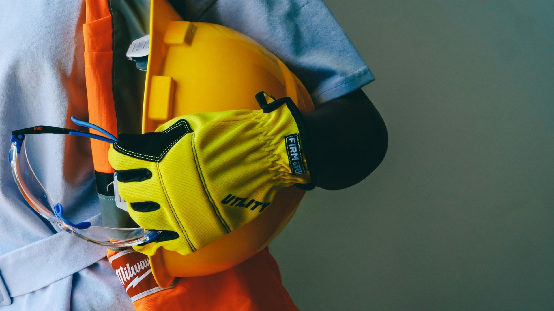 Worker in orange safety vest holding a yellow glove against a gray background