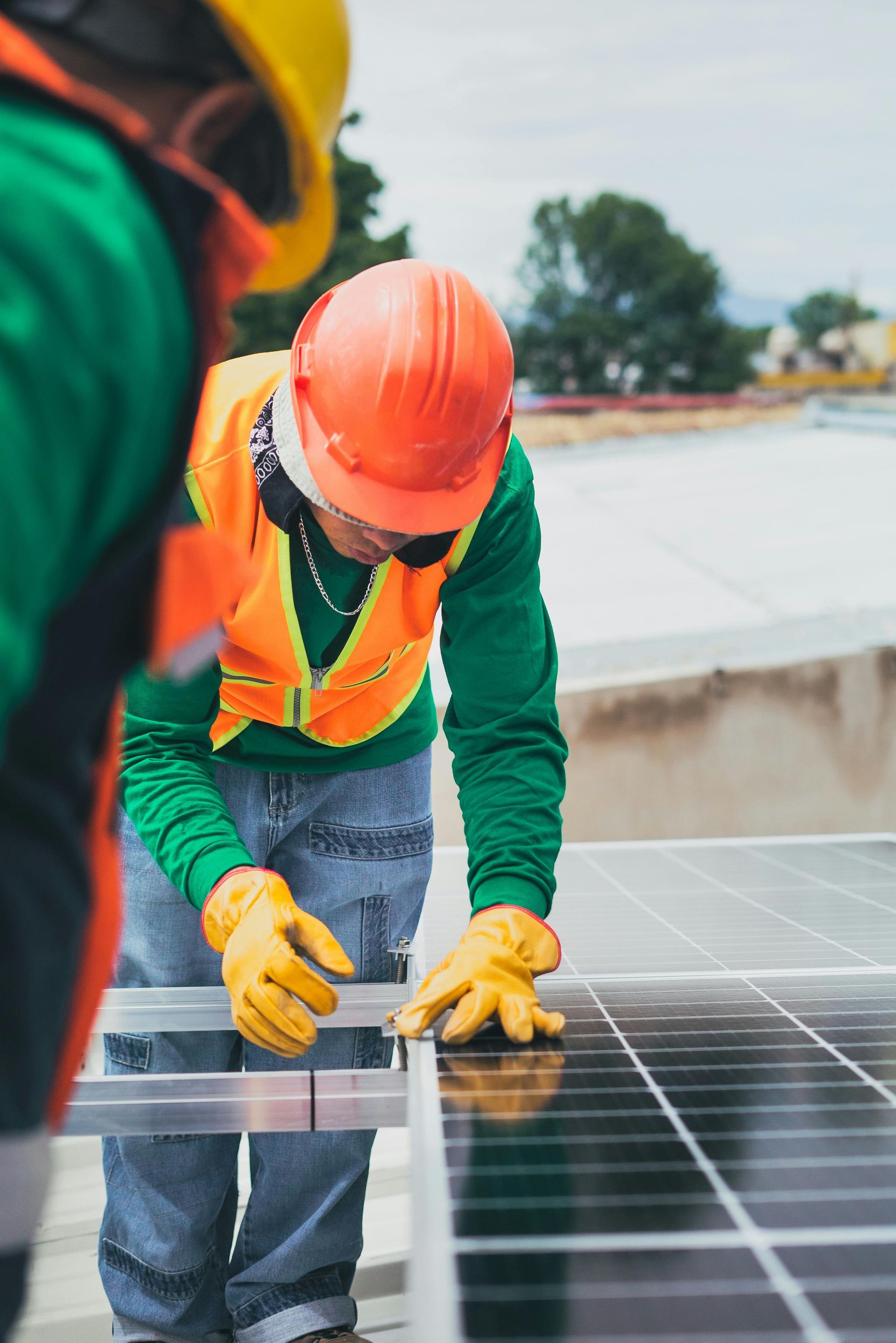 Worker in orange hard hat and safety vest installing solar panels on a rooftop