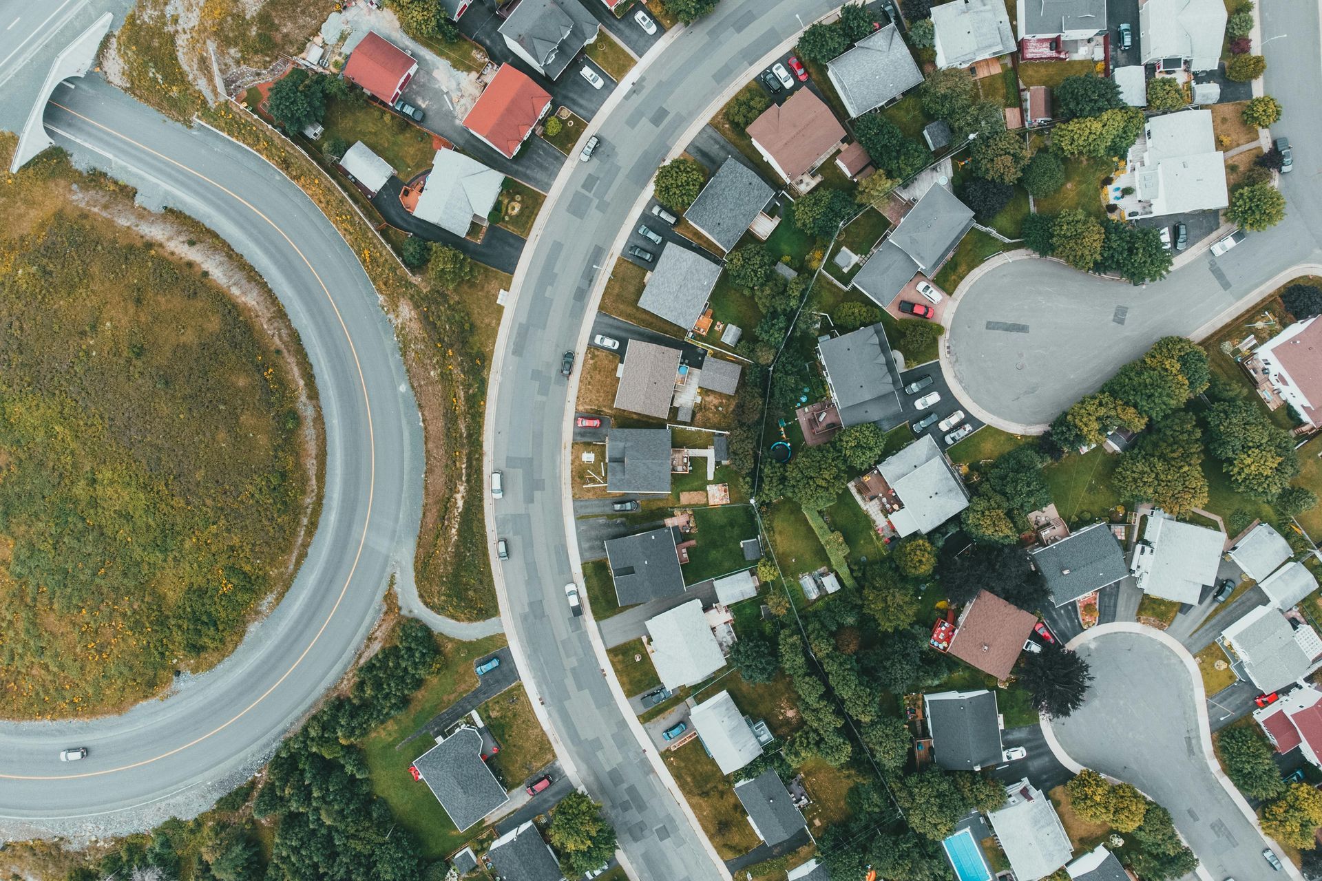 Aerial view of a curved suburban street with houses, trees, and a large roundabout.