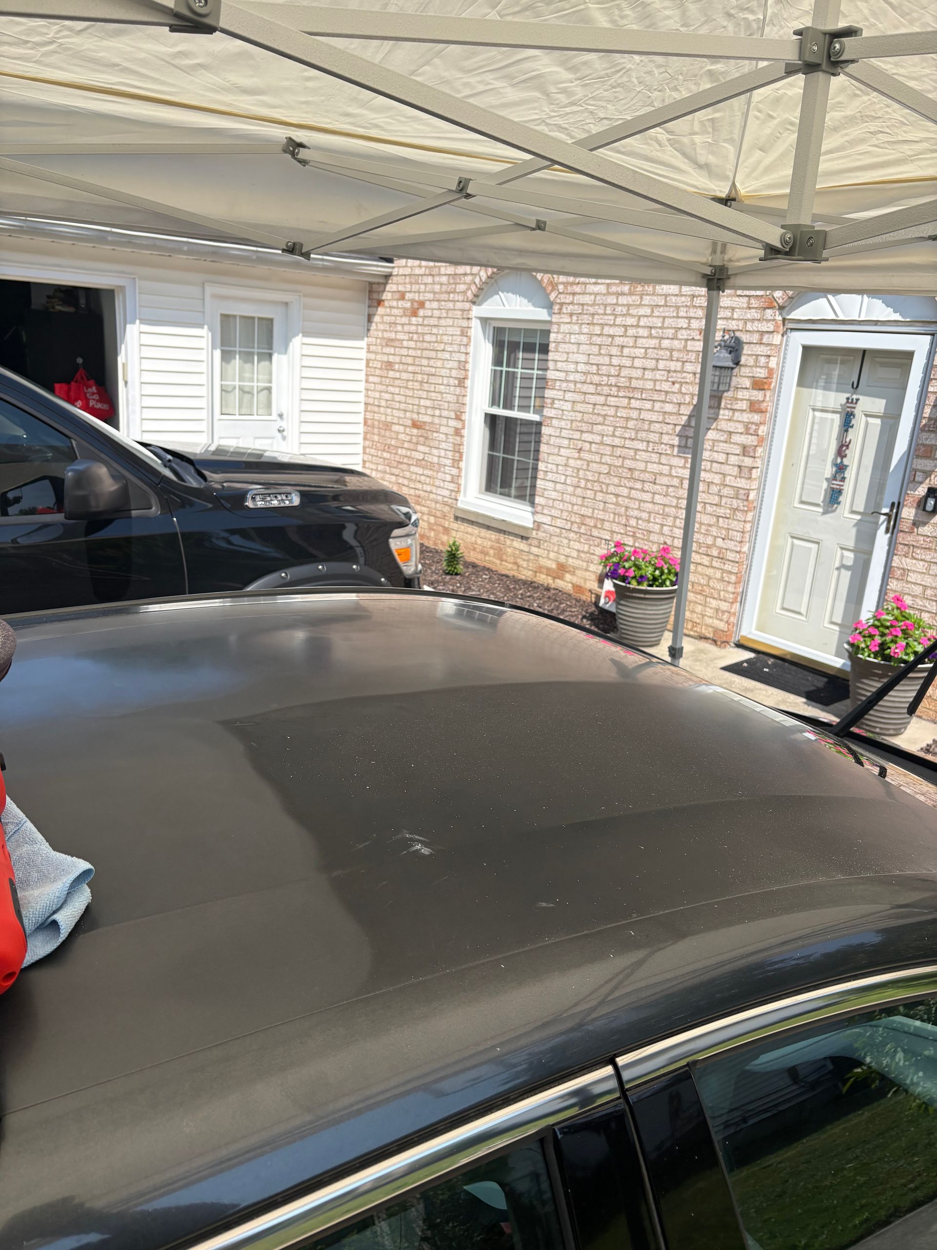 Black car roof under a white canopy, a red cloth is on the left, and a brick building is in the background.