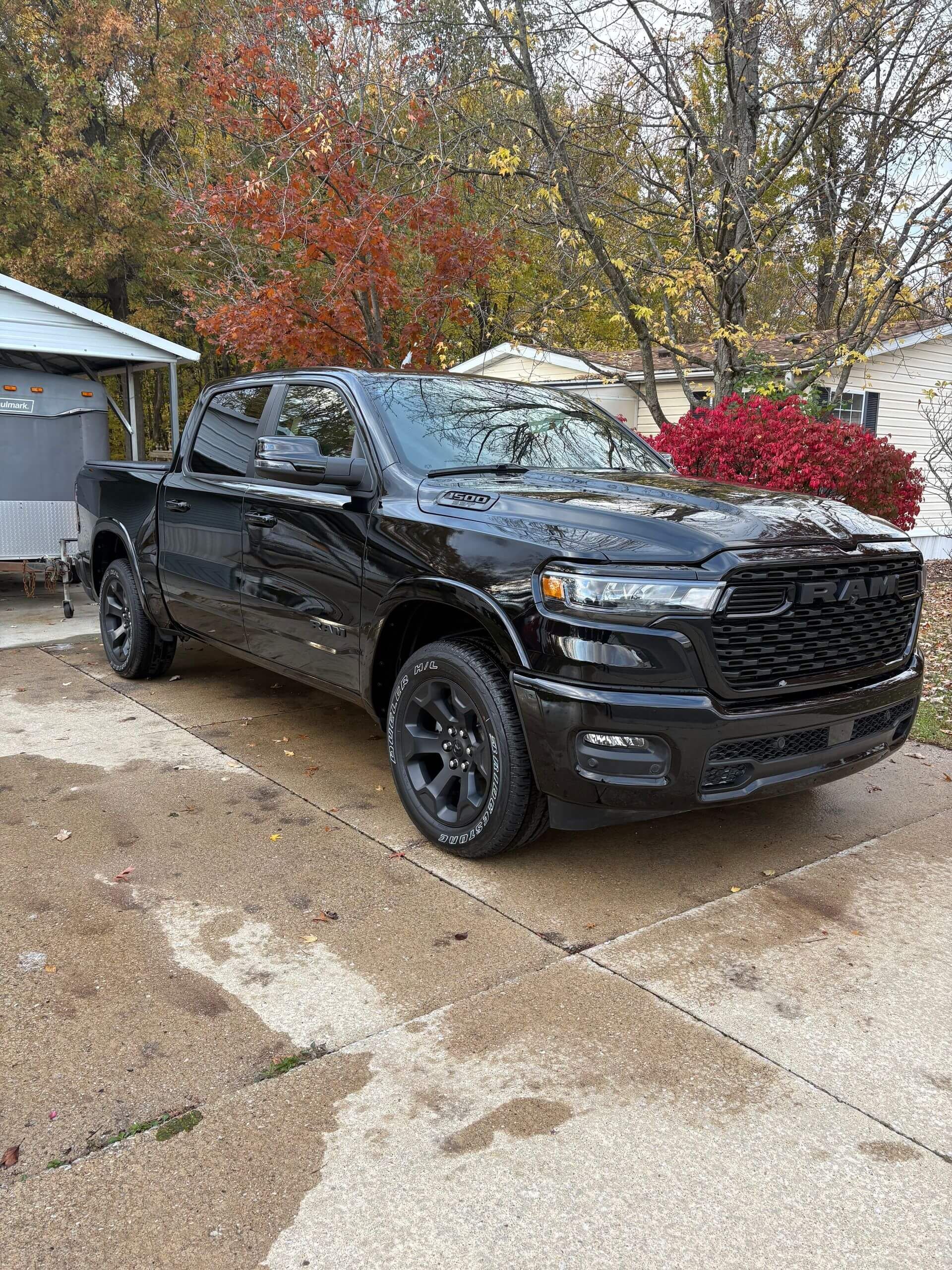 Black Ram pickup truck parked on concrete, surrounded by trees with fall foliage.