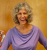 A Wendy LeBlanc-Arbuckle wearing a purple shirt and a microphone is smiling.