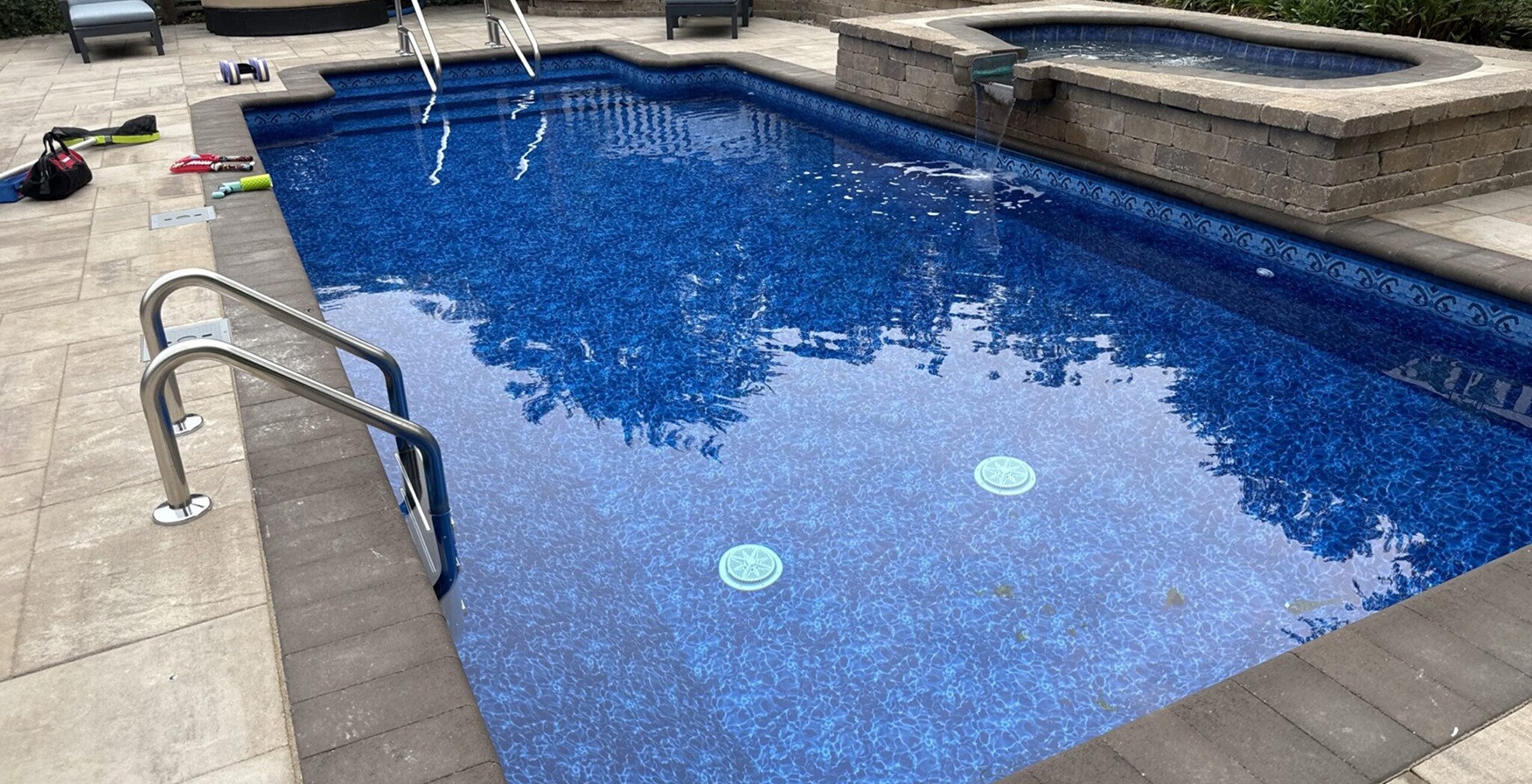 Rectangular blue swimming pool with metal handrail and stone deck beside it