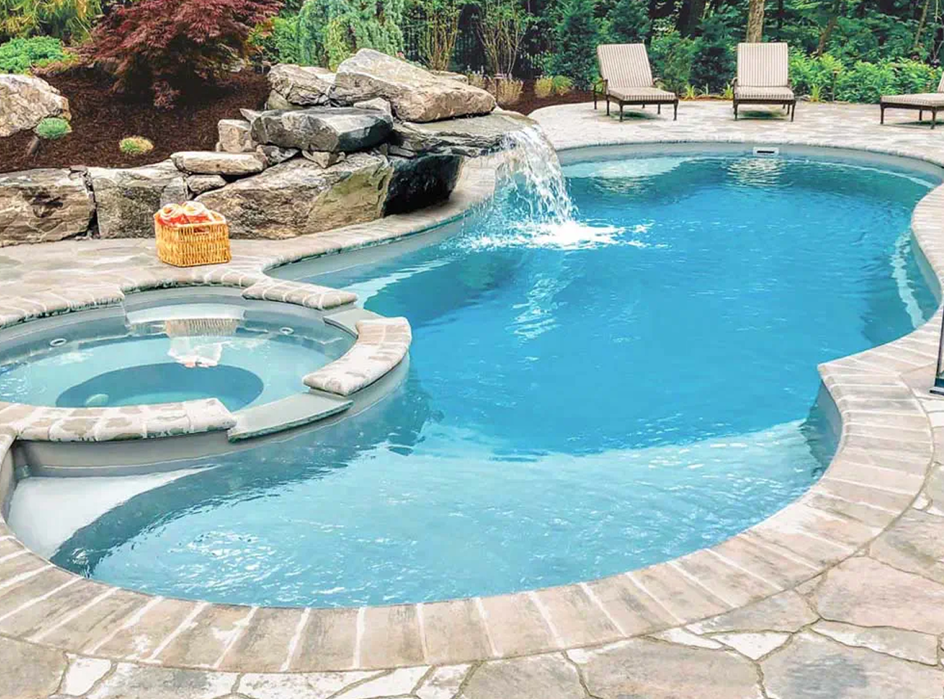Backyard pool with a spa, rock waterfall, and two lounge chairs on a stone patio