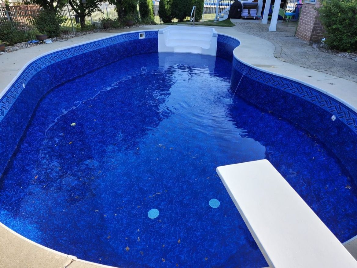 Small blue-tiled swimming pool with a white diving board and surrounding patio area