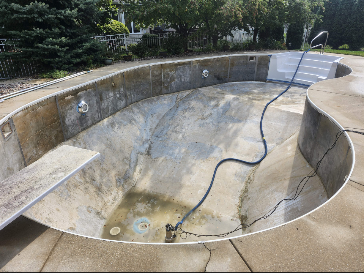 Empty drained swimming pool with a hose lying across the basin and steps at one end