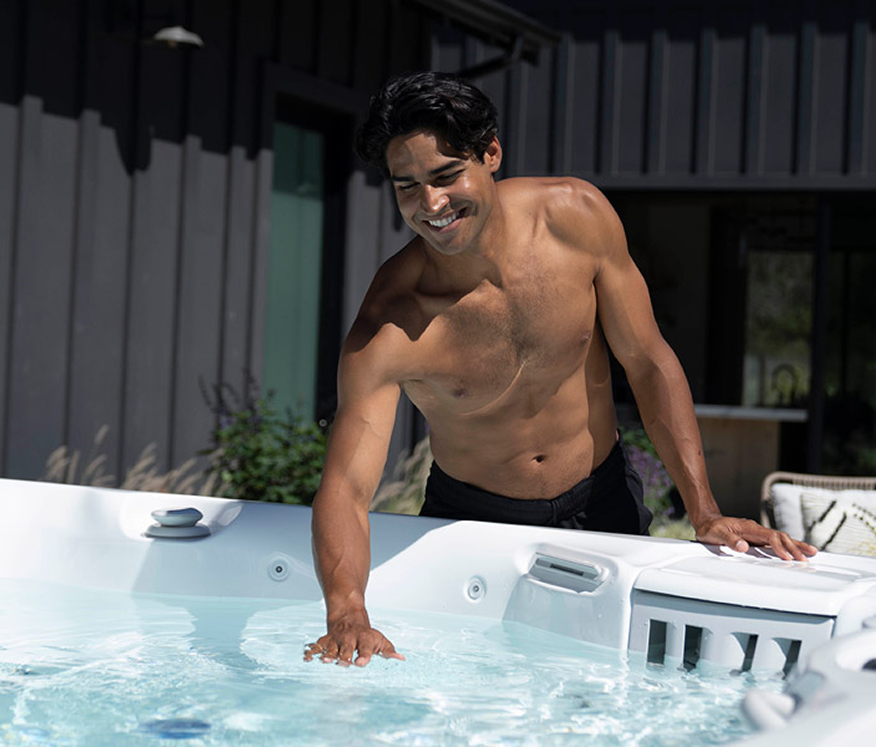 Man smiling in a hot tub, leaning on the edge in bright sunlight.