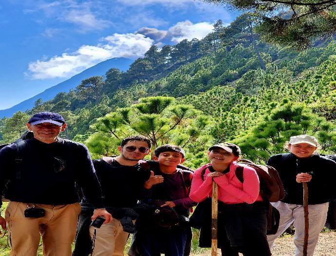 Cinco excursionistas posando en un sendero de montaña con exuberantes picos verdes y cielo azul de fondo.