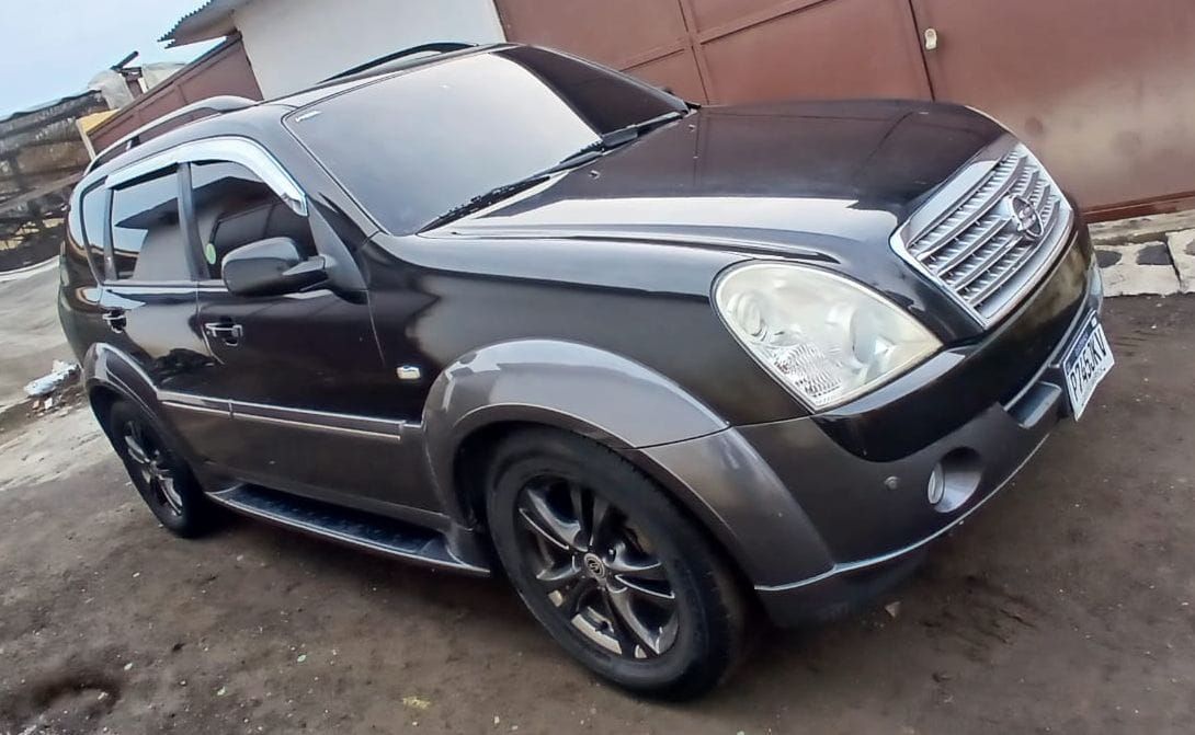 SUV negro estacionado en una calle mojada junto a un muro marrón, vista frontal en ángulo.