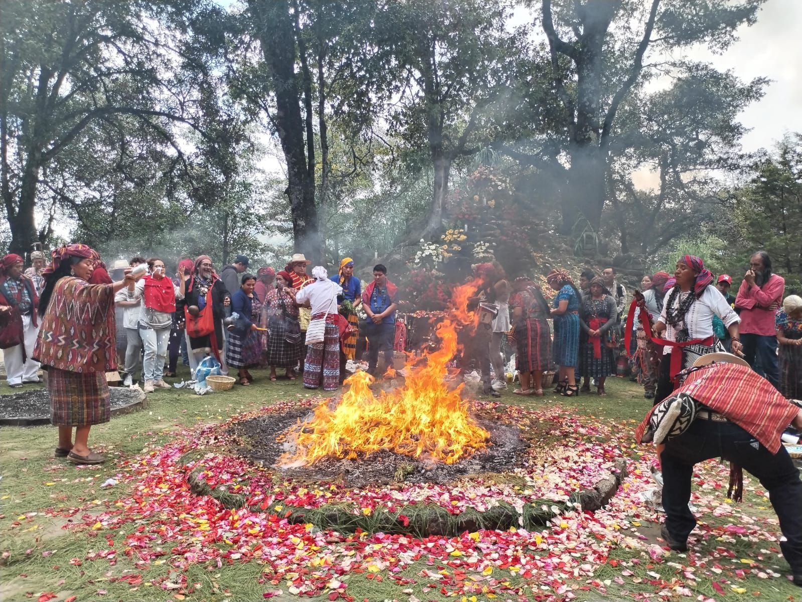 La gente se reunió al aire libre alrededor de una hoguera, con flores esparcidas en círculo sobre el suelo.