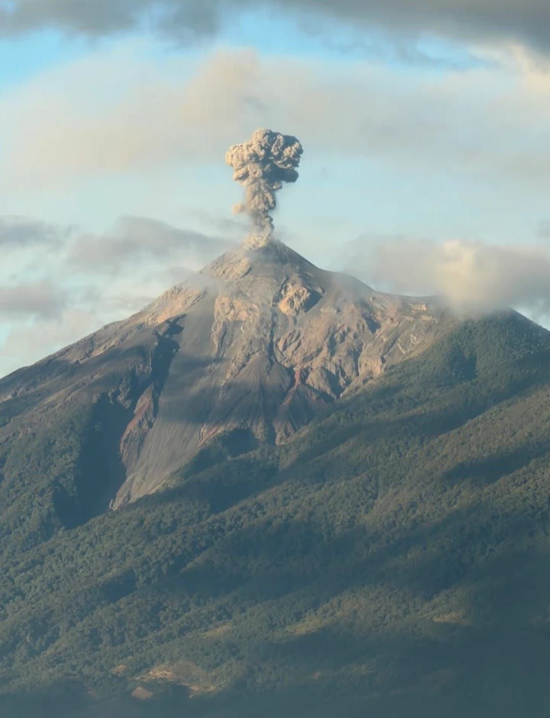 Columna de humo que se eleva desde un volcán en erupción bajo un cielo nublado.