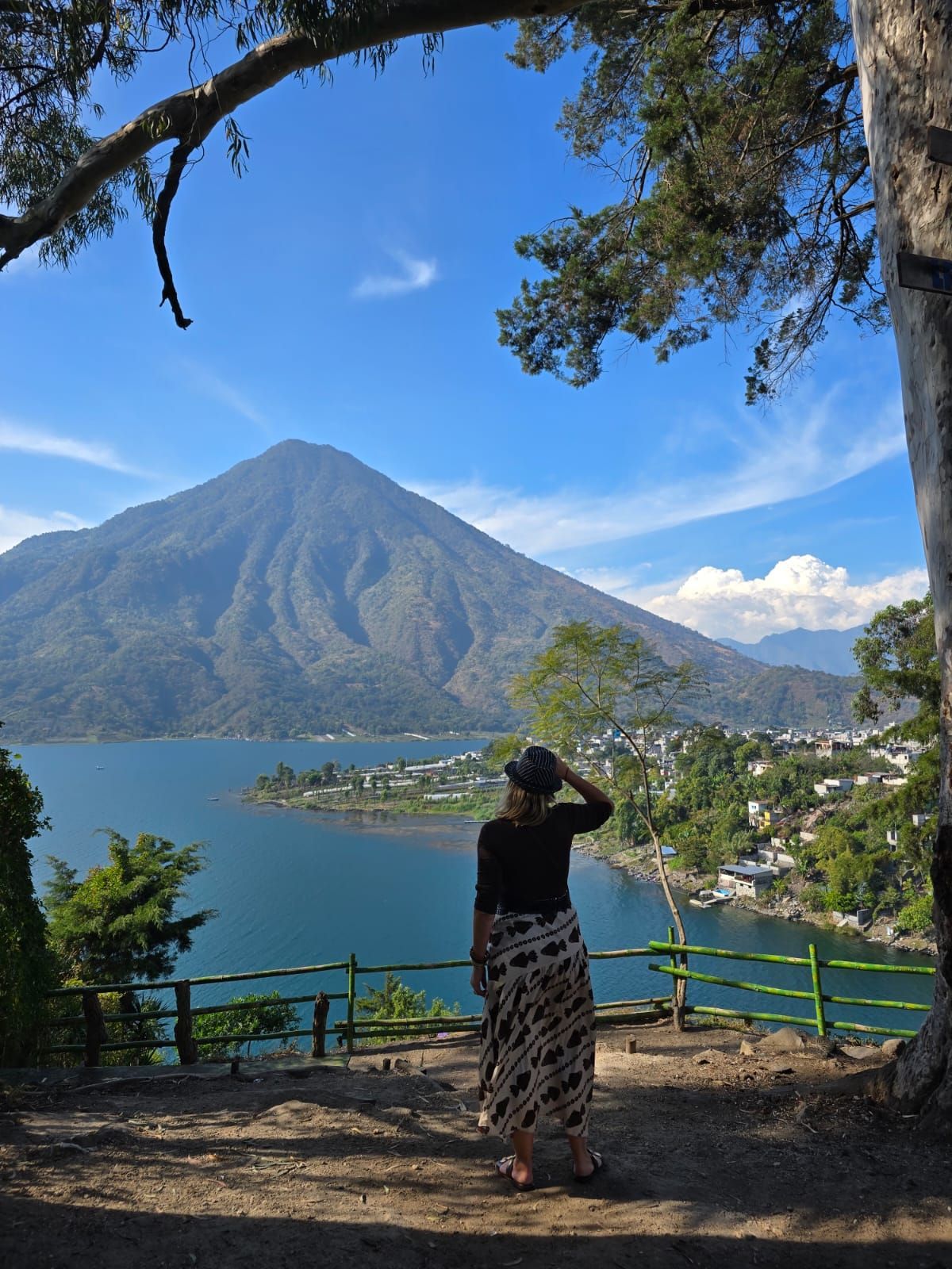 Persona contemplando un lago azul y una montaña volcánica desde un mirador sombreado.