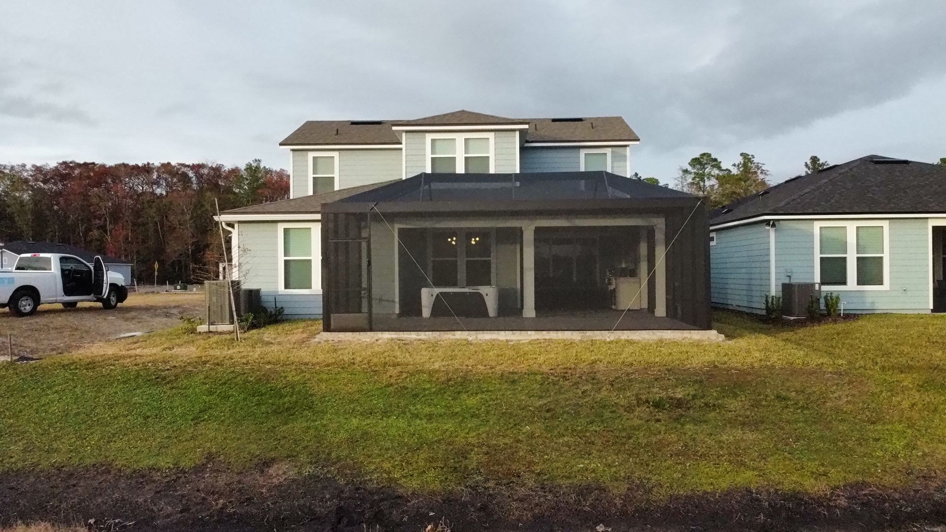 A two-story light blue house with a dark screen-enclosed patio, set in a grassy yard under a cloudy sky.