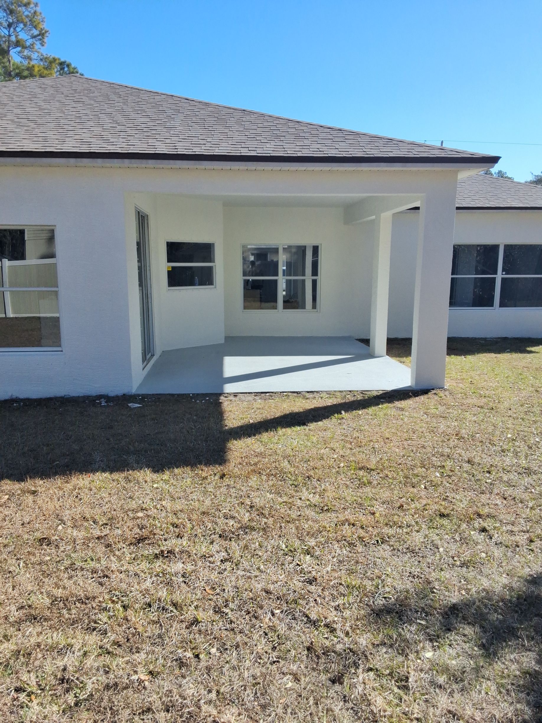 A white, single-story house exterior with a covered porch and brown roof, situated on a grassy lawn under a clear sky.
