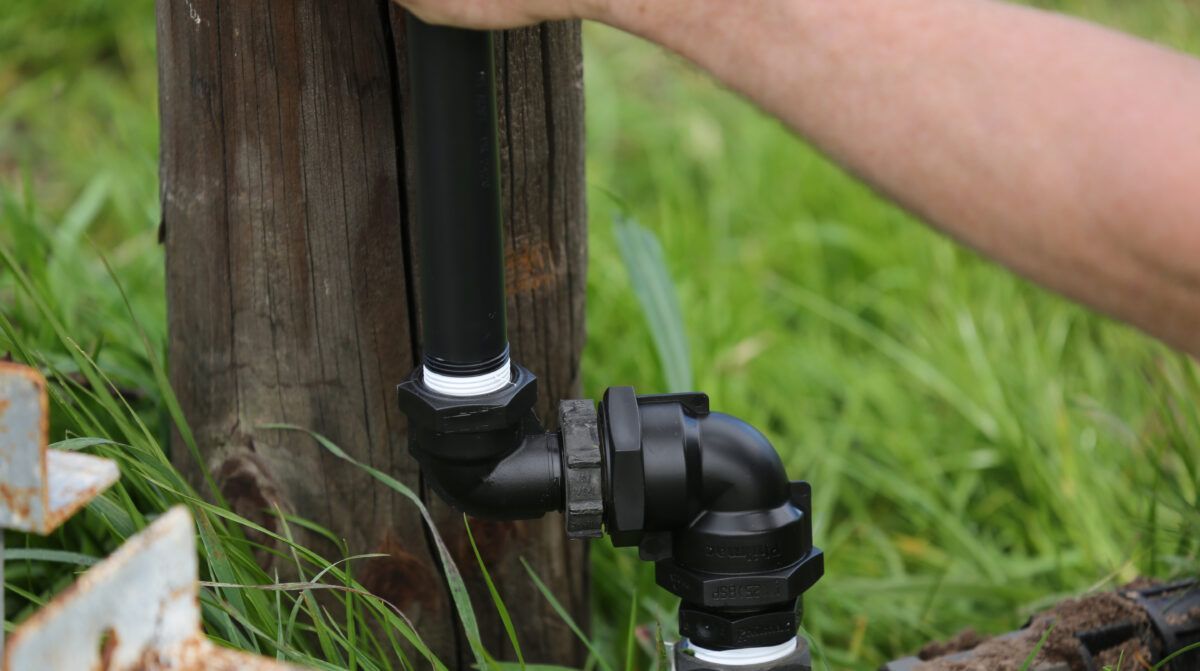 Black Irrigation Pipe and Elbow Connector Attached to a Wooden Post — Taree Water Works in Taree, NSW