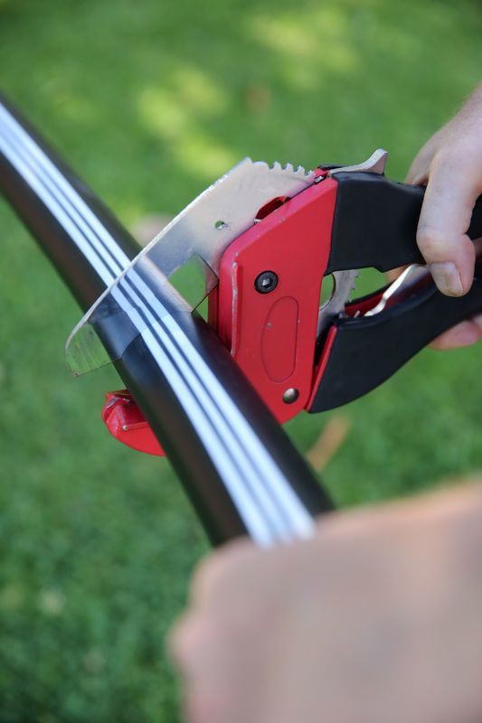 Hands Using a Red and Black Tool to Cut a White-and-blue Cable — Taree Water Works in Taree, NSW