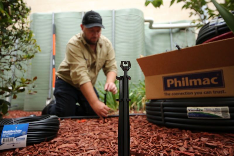 Worker Installing Black Cable Irrigation in a Garden Bed Beside a Philmac Box — Taree Water Works in Taree, NSW
