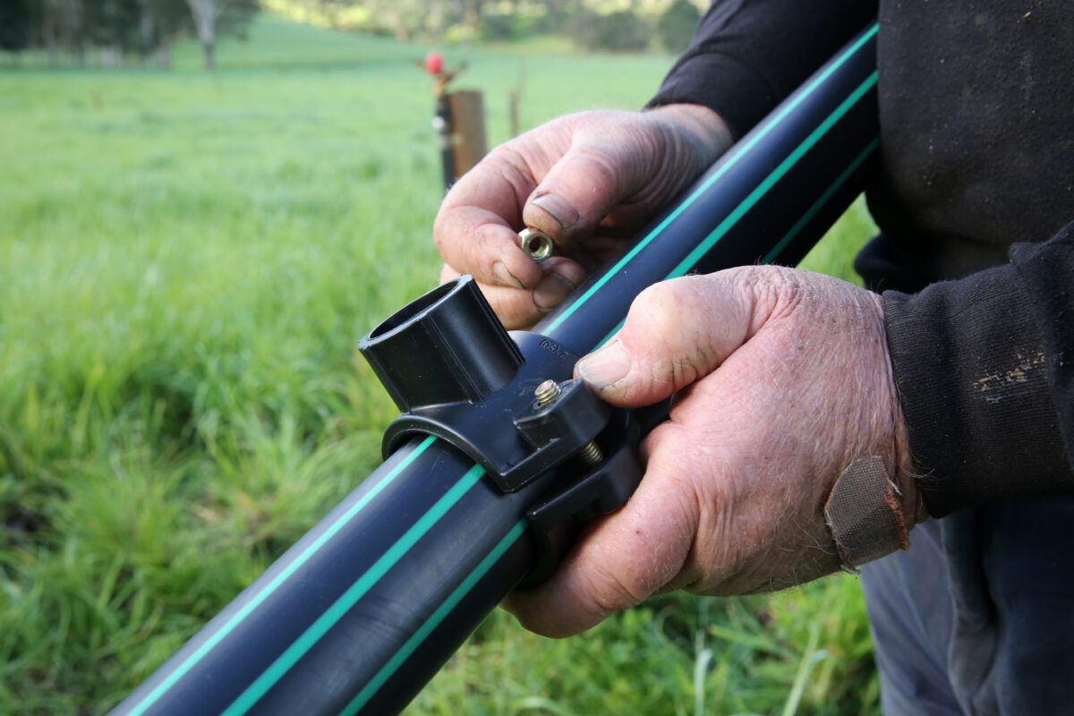 Hands Securing a Black and Blue Hose Clamp on a Pipe Outdoors in Grass — Taree Water Works in Taree, NSW
