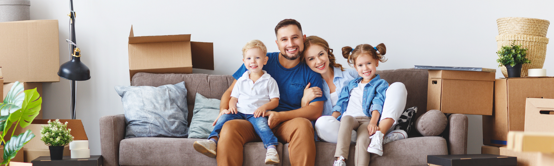 Family sitting on a gray couch among moving boxes in a bright living room