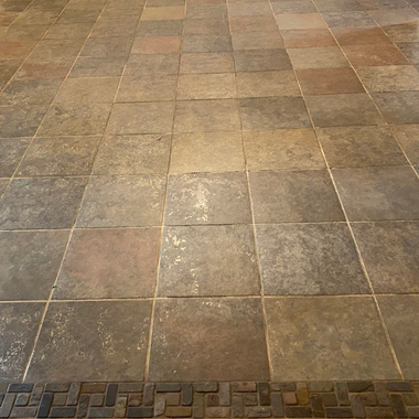 A stone-tiled floor with a warm, multicolored finish, accented by a narrow border of small rectangular bricks at the base.