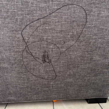Dark gray fabric upholstery marked with a black scribble or ink drawing.