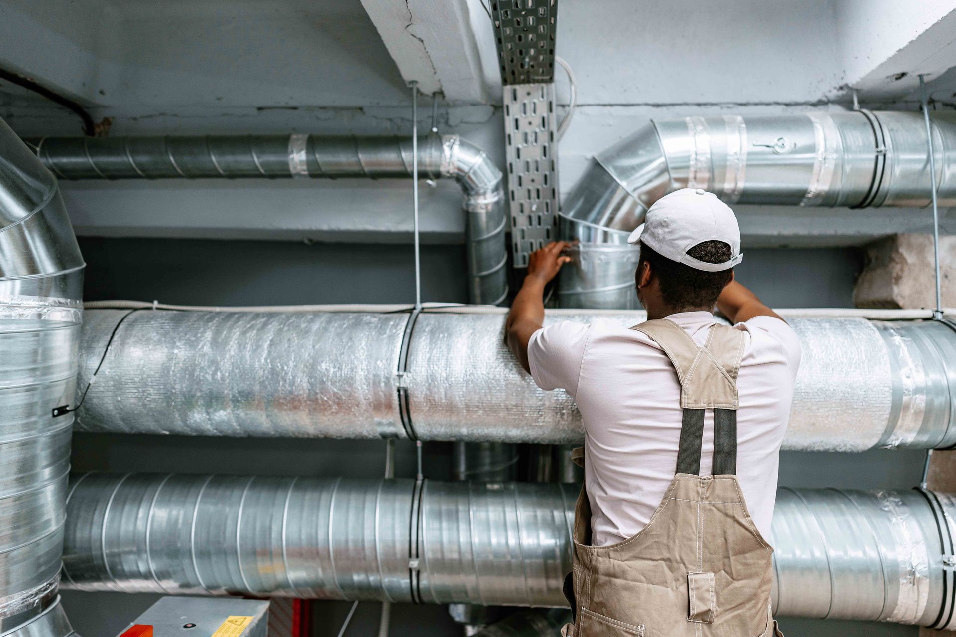 Worker inspecting large silver HVAC ducts in an industrial utility space