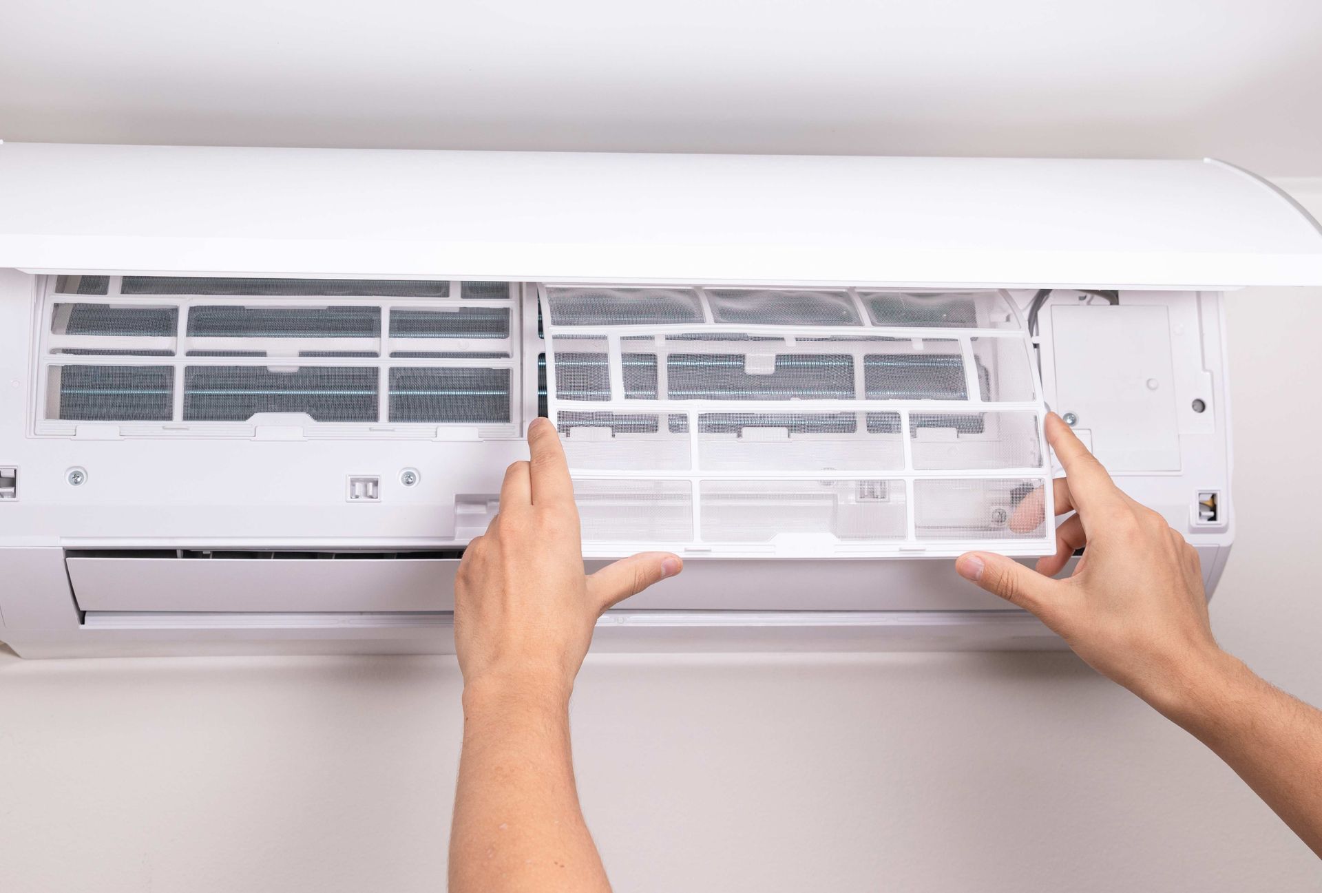 Hands cleaning the filter of a wall-mounted air conditioner