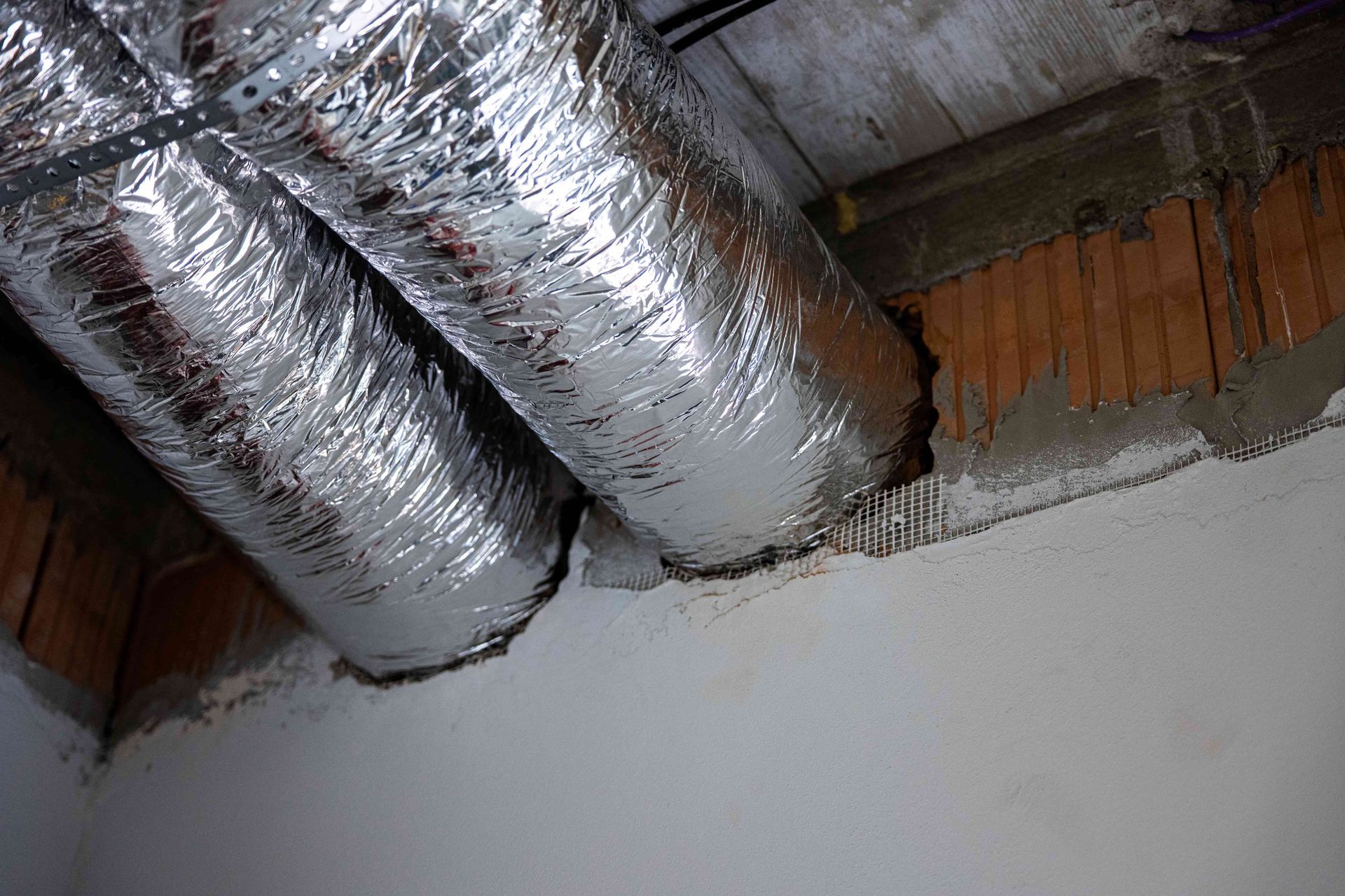 Foil-wrapped HVAC ducts above a white wall in an unfinished ceiling space