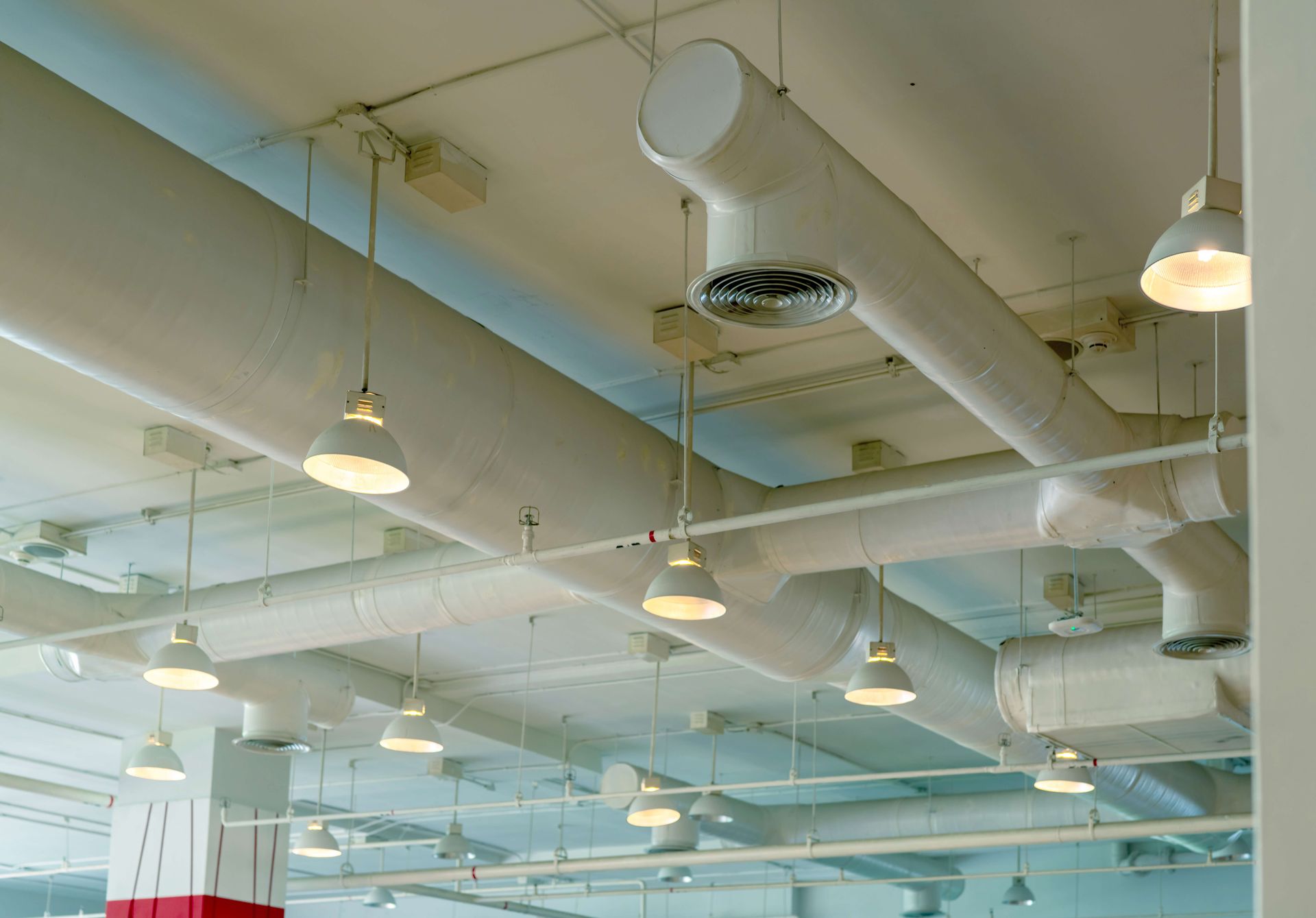 Industrial ceiling with white ducts, pipes, and hanging lights in a bright interior room
