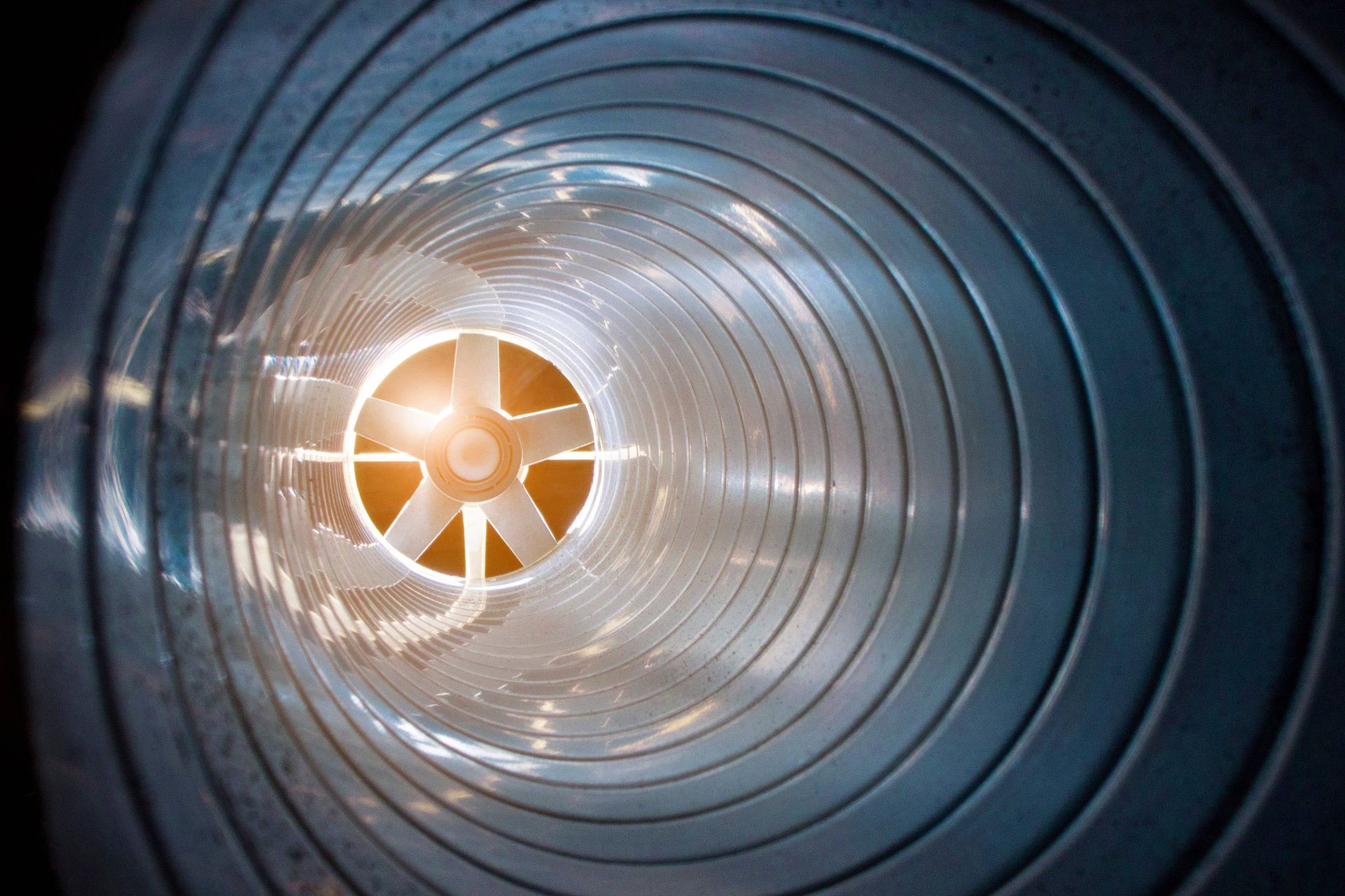 Inside a metal ventilation duct, a bright orange fan glows at the far end.