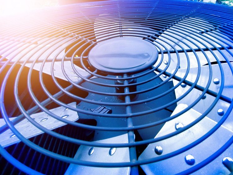 Close-up of a blue metal fan grille with circular vents and water droplets, lit by purple and orange light