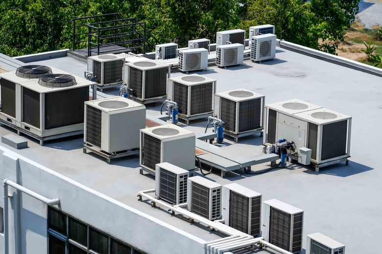 Rooftop HVAC units and vents on a flat commercial building roof surrounded by trees