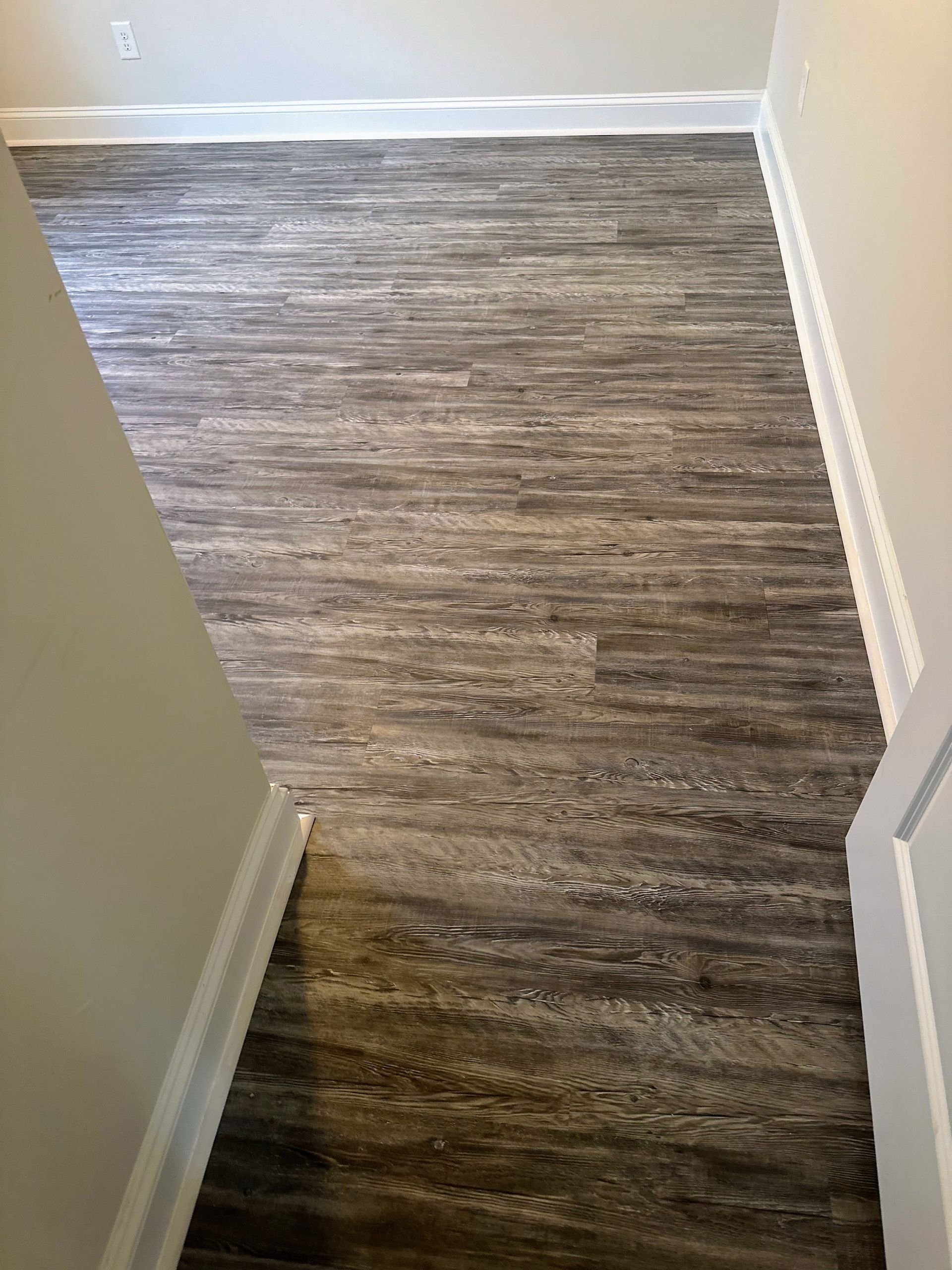 Dark wood-look flooring in a hallway with white trim and beige walls.