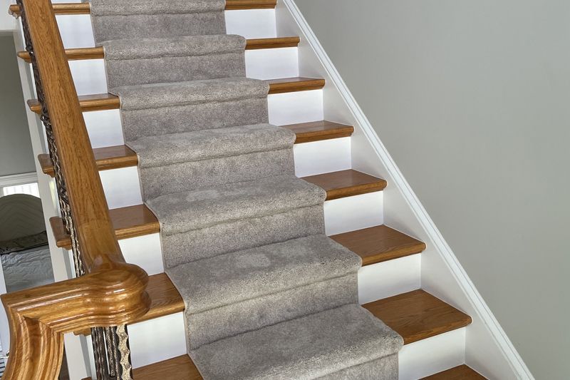 Staircase with wooden steps and railing, beige carpet runner, and white risers.