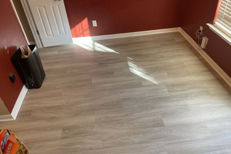 Room with light wood-look flooring, white trim, and maroon walls; a door and window are present.