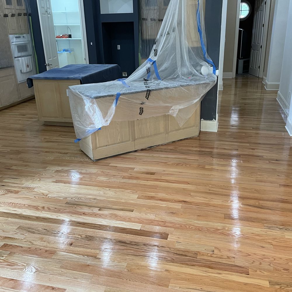 Newly refinished hardwood floors in a kitchen, cabinets covered in plastic.
