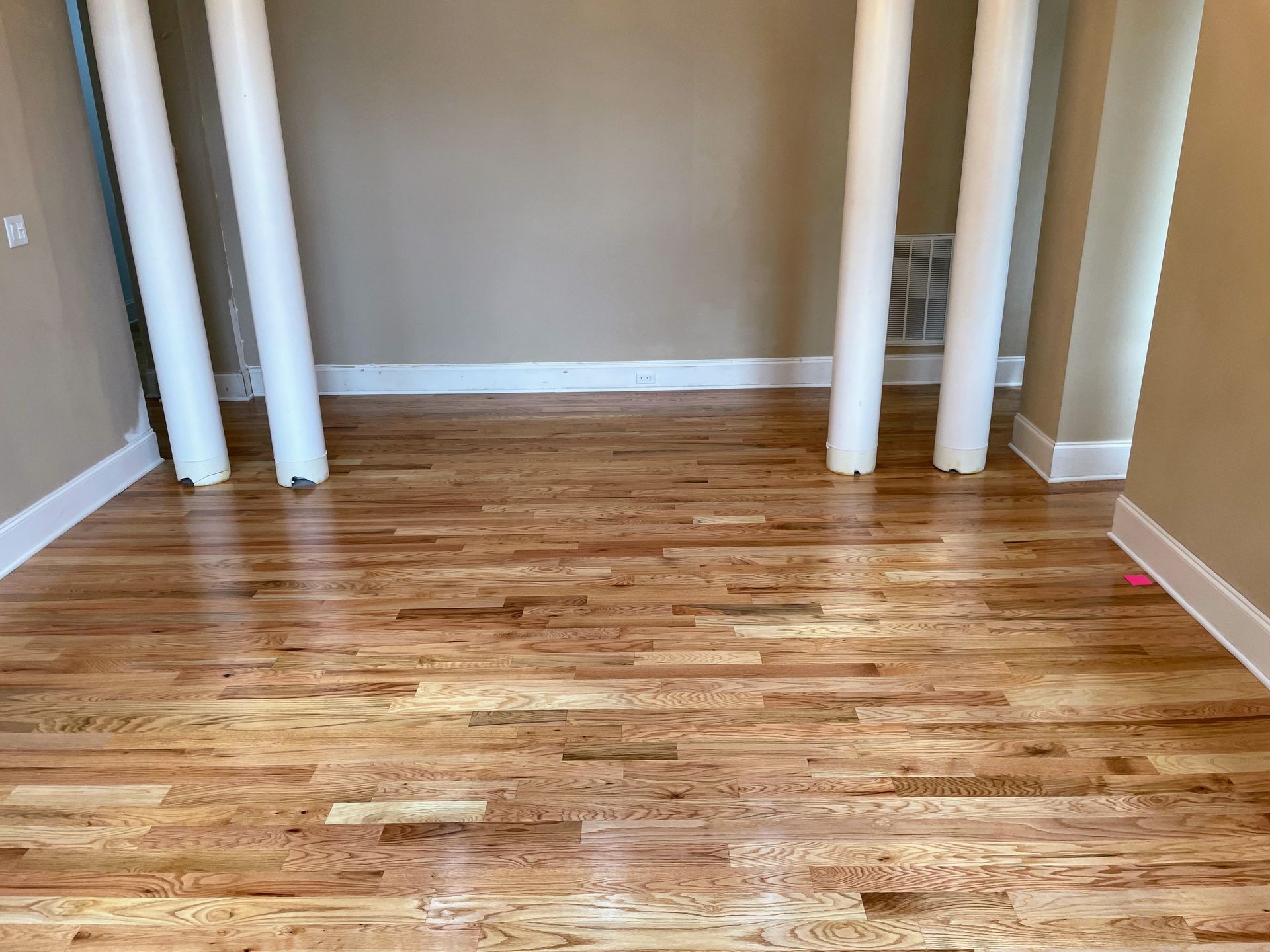 Wooden floor in a room with white columns, baseboards, and beige walls.