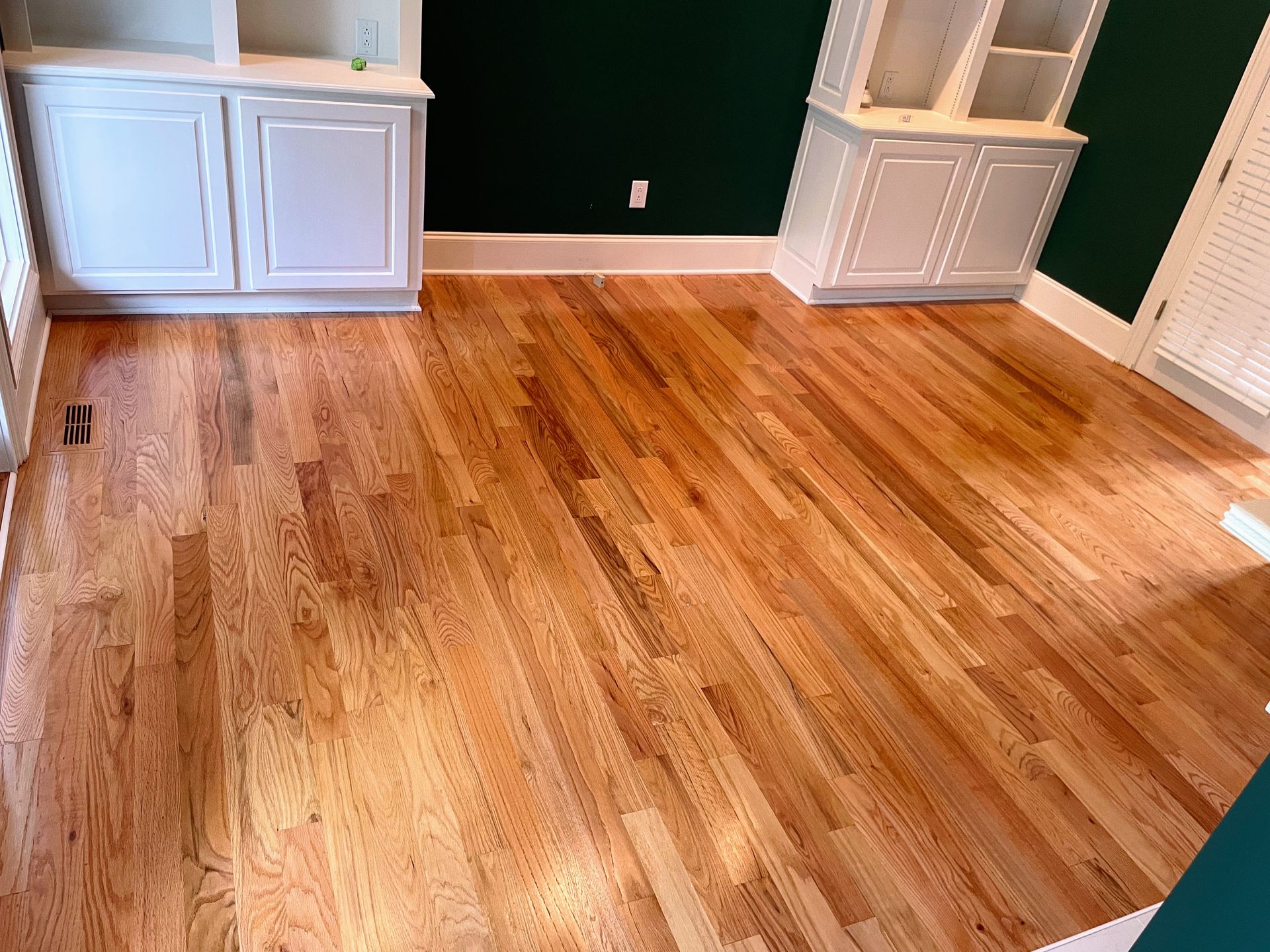 Hardwood floor with white cabinets and dark green wall.