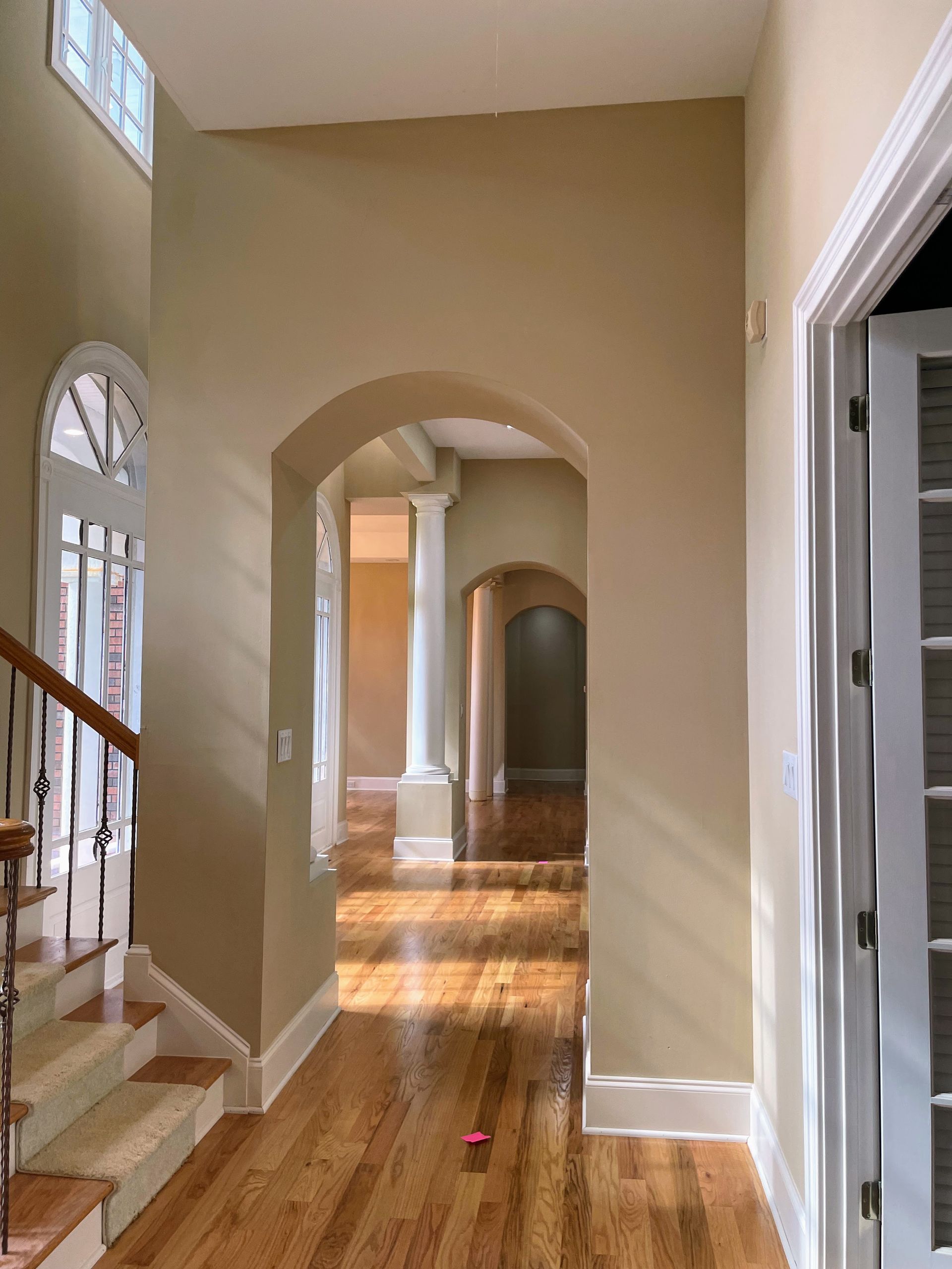 Hallway with hardwood floors, arches, and a staircase. Beige walls and white trim.