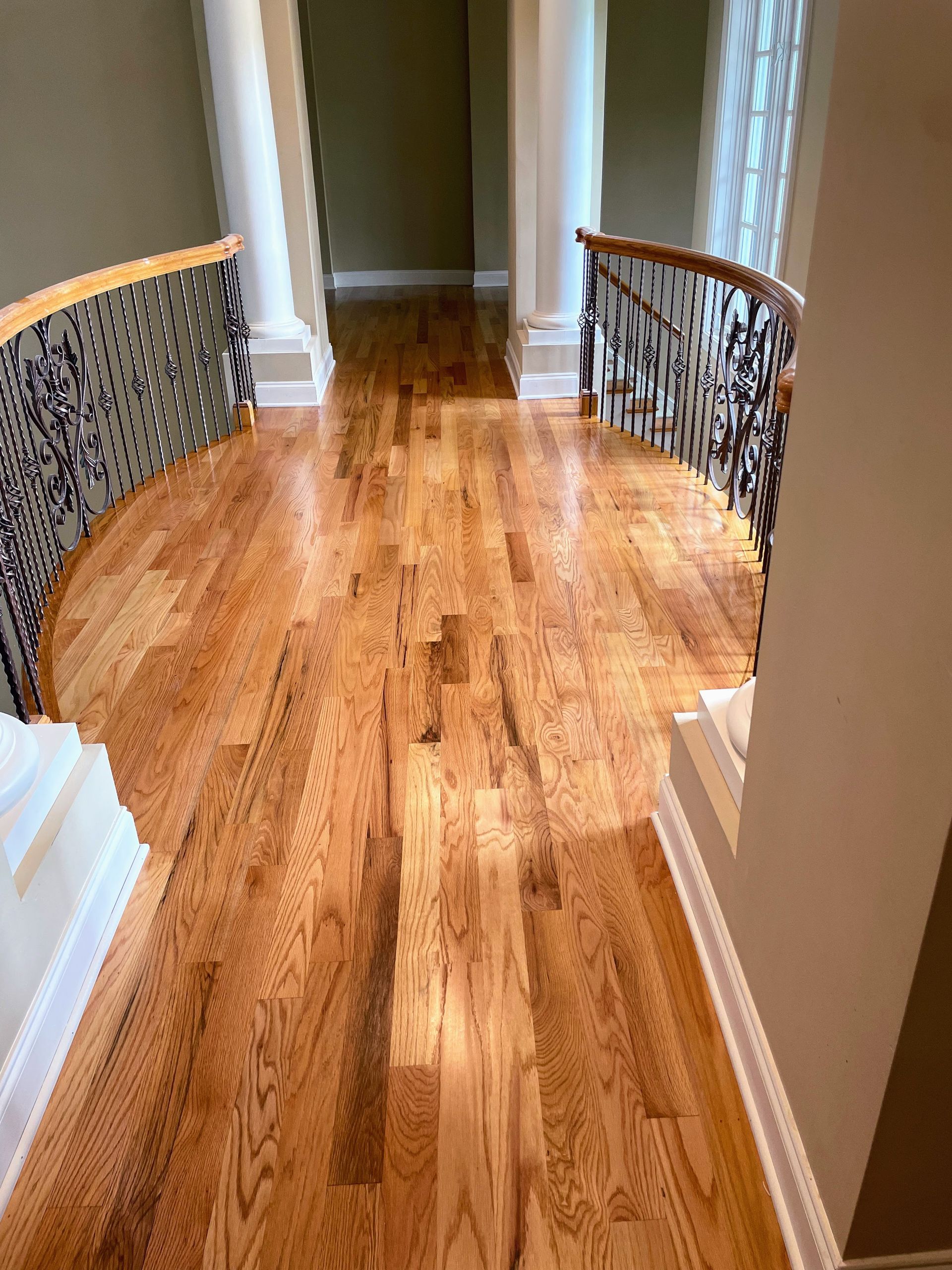Wooden hallway with ornate railings, architectural columns, and a view down a hallway.