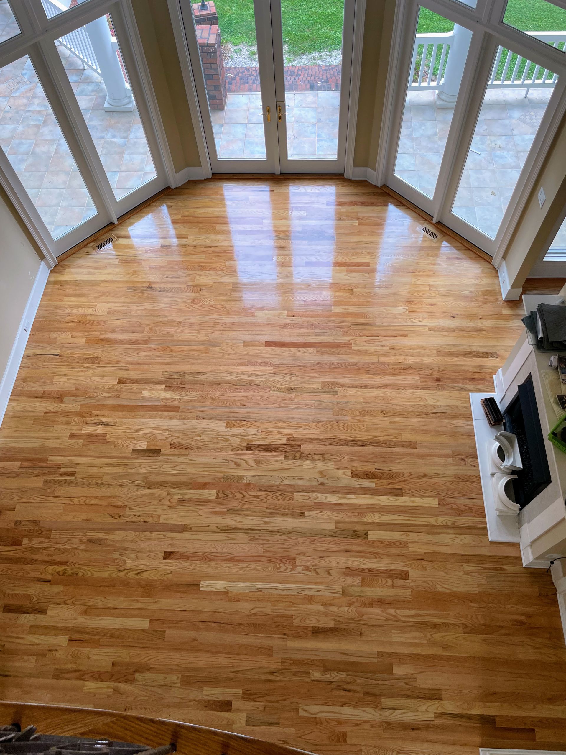 Hardwood floor in sunlit room with arched windows and fireplace.